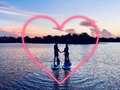 Couple on paddleboards on water holding hands looking at sunset